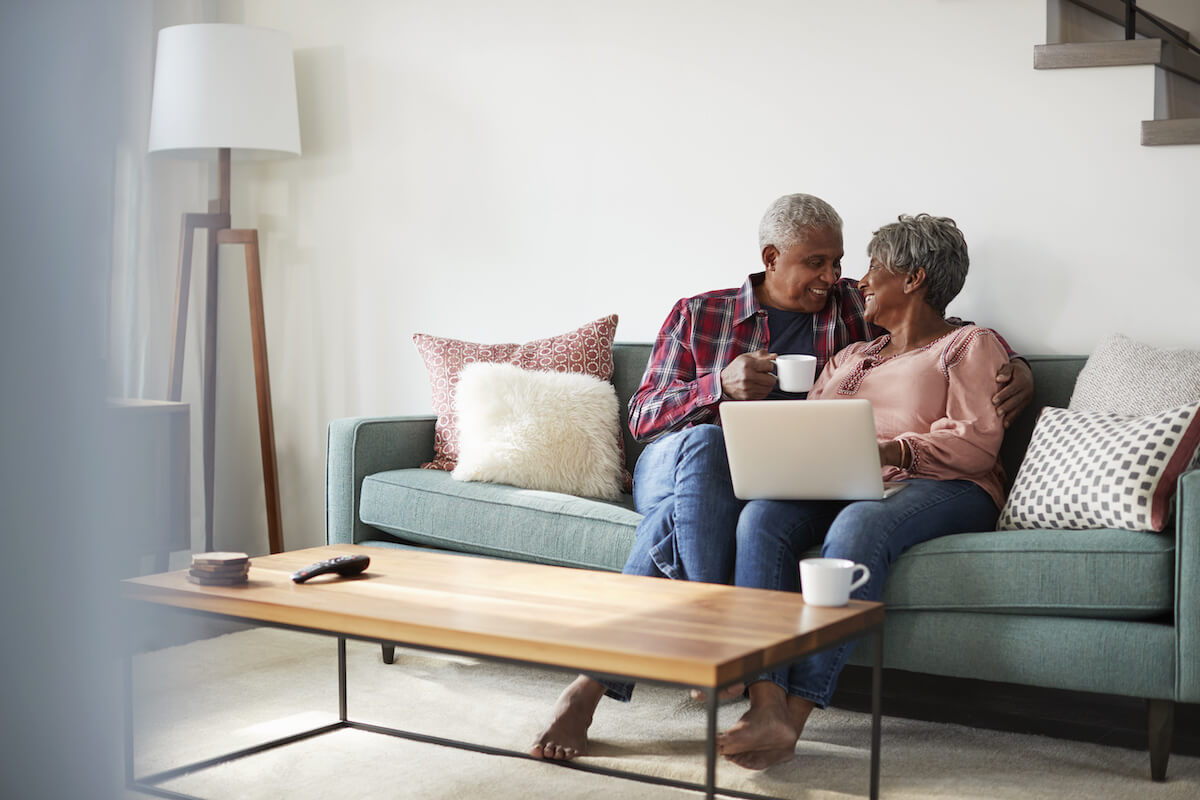 Buda Oaks | Happy senior couple sitting on thier couch looking at their computer while drinking coffee