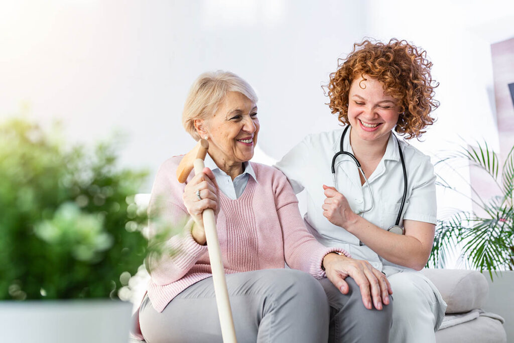 Buda Oaks | Friendly relationship between smiling caregiver in uniform and happy elderly woman. Supportive young nurse looking at senior woman. Young caring lovely caregiver and happy ward